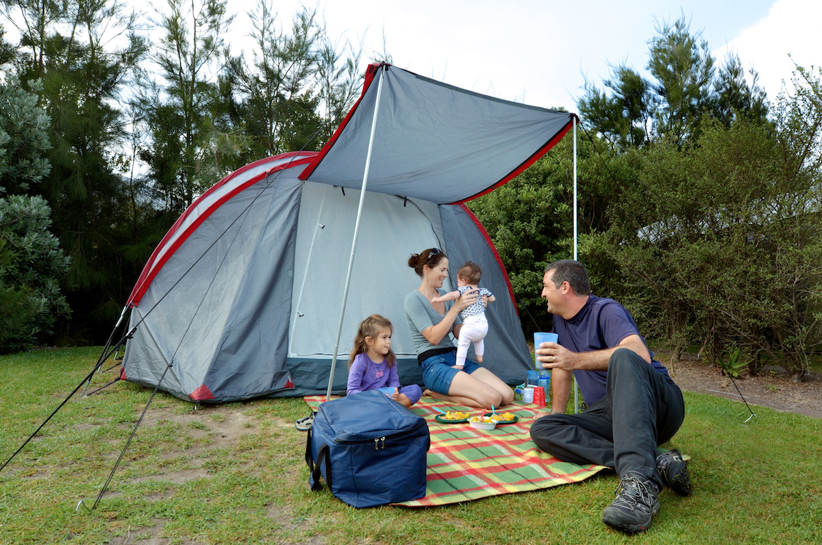 Young family, father and mother with two children camping in a tent outdoors.